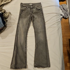 Grå bootcut jeans från Gina Tricot - Snygga grå lågmidjade jeans från Gina Tricot i bootcut-modell. Jeansen har klassisk femficksdesign med coola ficklock och silverfärgade knappar bak. Materialet är jeans i tvättad grå nyans, perfekt för en avslappnad och trendig look.