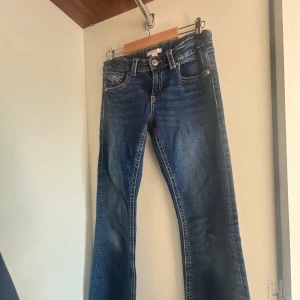 Blå bootcut jeans från Gina Tricot - Snygga blå jeans från Gina Tricot i klassisk bootcut-modell. Jeansen har fem fickor, markerade sömmar och knäppning fram. Perfekt tvättad denim med lätt slitning och coola bakfickor med lock och knapp.