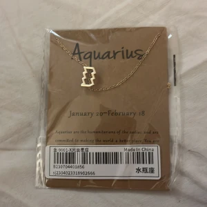 Guldigt halsband Vattumannen stjärntecken - Snyggt halsband i guld med ett minimalistiskt Vattumannen-symbolhänge. Kedjan är tunn och elegant, perfekt för dig som vill visa upp ditt stjärntecken på ett stilrent sätt. Passar perfekt som personlig accessoar eller present.