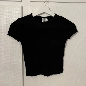 Svart ribbad croppad topp Gina Tricot - En svart, croppad topp från Gina Tricot med ribbad struktur. Modellen har korta ärmar och rund halsringning, perfekt för en clean och stilren look. Vid intresse eller frågor, skriv privat💕 