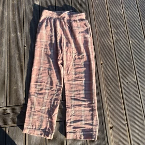 Rosa rutiga mjukisbyxor från Lager 157 - Mysiga rosa mjukisbyxor från Lager 157 med rutigt mönster och resår i midjan. Byxorna har raka ben och är tillverkade i ett mjukt bomullstyg, perfekta för chill dagar hemma. Klassisk loose fit och skön känsla hela dagen.