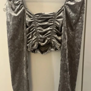 Grå sammetstopp med från H&M - Superfin croppad topp i grå sammet från H&M med långa puffärmar och snygga rynkade detaljer framtill. Toppen har en fyrkantig urringning och är perfekt för dig som vill sticka ut med en trendig look.