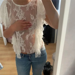 Vit spetsblus med volangärmar - Superfin transparent vit blus i spets med blommigt mönster och volangiga korta ärmar. Perfekt för dig som vill sticka ut med en romantisk och trendig look. Blusen har rund halsringning och är lätt och luftig. Har även i rosa på annan annons❤️