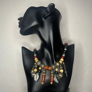 Vintagehalsband med karneol, jaspis och metall – retro, boho & tribal vibe -  Färgstarkt vintagehalsband med stora pärlor i trä, metall och sten. Karneol-liknande orange pärlor och melerad jaspis kombineras med lövdetaljer och bohemisk design. Troligtvis från 80-/90-talet. Längd: ca 45–48 cm. Mycket gott skick. Ingen prutning, men bra rabatt vid köp av flera. Jag rensar smyckesskrin och garderob – spana in mina andra annonser!  ⸻  