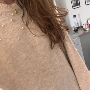 Beige stickad tröja med pärlor  - Superfin beige stickad tröja från H&M med pärldetaljer över bröstet och axlarna. Tröjan har rund halsringning och långa ärmar, perfekt för att ge en söt och trendig touch till din outfit. Superbra skick och stretchiga material. Så skön🤗