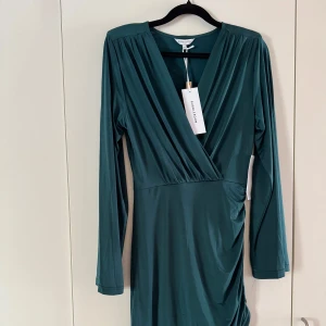 Mörkgrön omlottklänning Bubbleroom - Supersnygg mörkgrön omlottklänning från Bubbleroom med lång ärm och v-ringning. Klänningen har draperad detalj i sidan och är i ett mjukt, tunt material💚