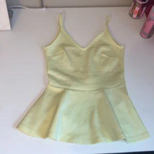 Gult volanglinne - Supersöt ljusgul linne-topp med smala axelband och v-ringning. Toppen har en volang nertill.