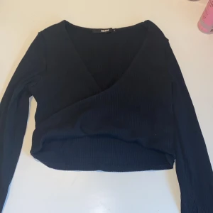  Omlottopp från Bik Bok - Svart croppad omlottopp från Bik Bok i ribbad bomullsmix. Djup v-ringning och långa ärmar ger en clean och stilren look. 