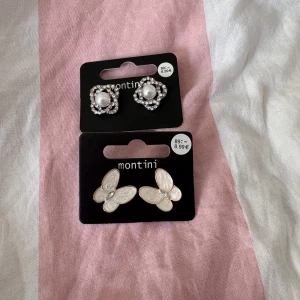 Fyra par örhängen från Montini & Ur&Penn - Säljer fyra par örhängen! Två från Montini: ett par med pärlor och gnistrande stenar i silver, och ett par vita fjärilar med guldkant och liten sten. Två från Ur&Penn: ett par små glittriga stenar och ett par vita blommor med gulddetalj. Perfekta för att mixa och matcha!