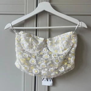 Blommig korsettopp - Superfin vit korsettopp från Zara med broderade blommor i vitt och gult. Helt oanvänd!