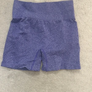 Lila seamless träningsshorts M - Snygga lila seamless shorts i stretchigt material med hög midja. Perfekta för gymmet eller löpning, med ventilerande detaljer längs sidorna. Tillverkade av polyamid, polyester och elastan för maximal komfort och rörelsefrihet.