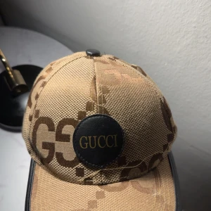 Beige keps med olika mönster  - En väldig fin beige keps med olika mönster och med en logga på framsidan, bra skick 