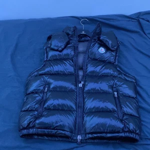 Svart dunväst från Moncler med huva - Säljer en svart, glansig dunväst från Moncler med avtagbar huva och två dragkedjefickor framtill. Västen har klassisk quiltad design och Moncler-logga på bröstet. Perfekt för lager-på-lager och riktigt snygg till streetwear. 1 :   1.     Nfc tag fungerar 