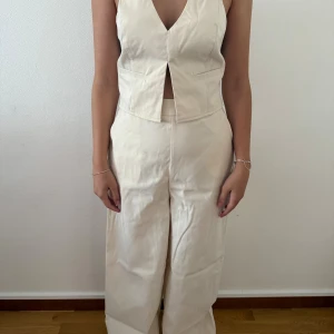 Vida beige byxor med övredel med snörning och öppen rygg - Snygga vida byxor i beige med hög midja och övre del en rak och loose passform med croppad längd. Perfekta för en clean och trendig look, tillverkade i ett mjukt bomullsmaterial.