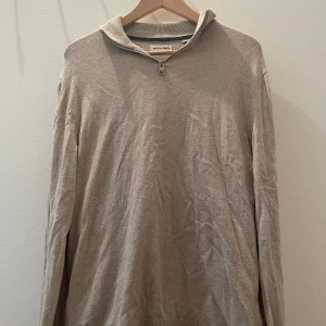 Beige half zip tröja Jack & Jones - Beige långärmad tröja från Jack & Jones med half zip-dragkedja vid halsen. Tröjan har en enkel och clean design, perfekt för lager-på-lager och chill vardagsstil. Tillverkad i mjukt bomullsmaterial för skön känsla.
