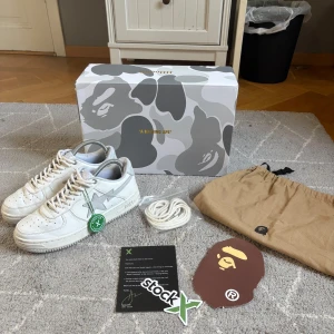 Vita BAPE STA sneakers från A Bathing Ape x JJJJound - Säljer ett par vita BAPE STA sneakers från A Bathing Ape. Skorna har klassisk låg siluett, stjärndetalj på sidan, snörning och präglad BAPE-logga på sulan. Tillverkade i skinn och levereras med originalkartong, extra skosnören, dustbag och BAPE-tag. Stock X verifiering följer även med. Skorna är i fint skick. Det är en collab med Bape och JJJJound.