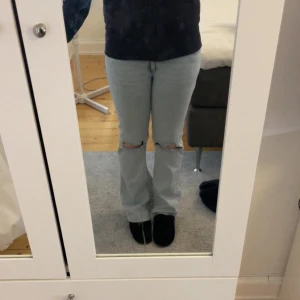 Ljusblå bootcut jeans med slitningar nelly - Säljer ett par ljusblå jeans med bootcut-modell och slitna hål på knäna. Jeansen har klassisk femficksdesign och coola broderade detaljer på bakfickorna. Sytt upp ungefär 5cm