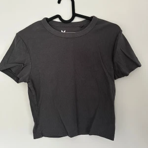 Mörkgrå ribbad t-shirt - Snygg mörkgrå t-shirt i ribbad bomull med rund hals och korta ärmar. Modellen är croppad 