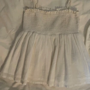 Supersöt vit topp - Supersöt vit topp från Gina Tricot. Är i storlek 146/152 men passar mig som brukar ha xs. Endast använd en gång och är i mycket bra skick. Man kan även ta bort axelbanden helt om man hellre skulle vilja ha den utan eller för att variera lite. 