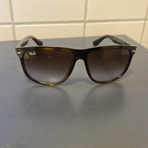 Ray-Ban bruna solglasögon - Snygga solglasögon från Ray-Ban med brunmelerad plastbåge och stora fyrkantiga glas. Glasen är mörktonade och ger en cool look. Klassisk Ray-Ban-logga på både lins och skalmar. Perfekta för soliga dagar och streetstyle.