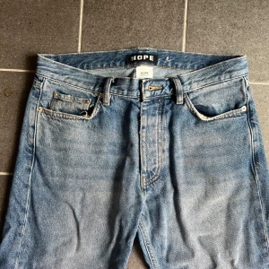 Hope Rush Denim - Säljer ett par klassiska blå jeans från HOPE, modell WORK. Jeansen har rak passform, fem fickor och snyggt tvättad denim. Perfekta för dig som gillar en tidlös look med lite loose fit. Tillverkade i bomull och har coola slitningar för extra edge. Har sprättat upp sömmarna längst ner då jag ville ha de lite längre! 
