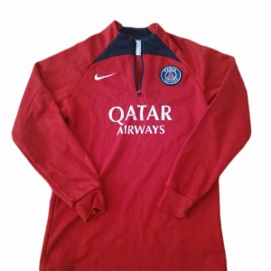 PSG Nike Training Top – Red - PSG Nike Training Top – Red (XXS) Official Paris Saint-Germain long sleeve training top by Nike. ✔️ Size: XXS ✔️ Color: Red with black and white details ✔️ Half-zip collar ✔️ PSG crest + Qatar Airways sponsor print ✔️ Comfortable fit, perfect for training or casual wear  ✅ Authentic Nike product ✅ Good condition (see photos)  💰 Price: 275 kr
