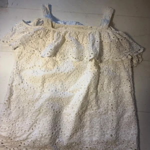 Vit broderad blus från Holly & Whyte - Superfin vit blus med broderade detaljer och volang upptill från Holly & Whyte. Blusen har breda axelband och ärmlös design, perfekt för soliga dagar. Materialet är mjukt och luftigt bomull med snygg spets och hålmönster som ger en romantisk vibe.