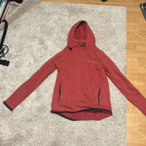 Röd hoodie från Klättermusen - Röd hoodie från Klättermusen med långa ärmar, huva med snörning och två fickor. Perfekt för kyliga dagar och outdoor-aktiviteter. Tillverkad i mjukt bomull som känns skönt mot huden.