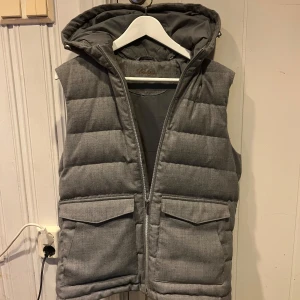  Stenströms väst - Snygg grå dunväst från Stenströms med quiltad design och avtagbar huva. Västen har två stora fickor framtill med lock och dragkedja hela vägen. Perfekt för lager-på-lager under kyliga dagar.