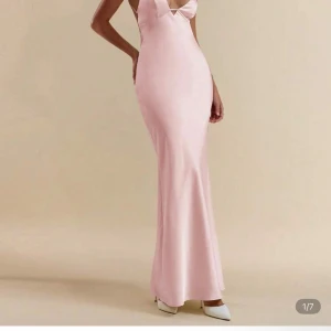 Ljusrosa långklänning i satin - Elegant ljusrosa långklänning i satin med v-ringad urringning och figurnära passform. Den har även en öppenrygg. Klänningen har smala axelband och en mjukt svepande siluett som ger en lyxig känsla. Perfekt för speciella tillfällen när du vill sticka ut. Aldrig använt! 