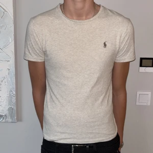 Beige t-shirt från Polo Ralph Lauren - Knappt använd snygg beige t-shirt från Polo Ralph Lauren med klassisk rund hals och brunt broderat logotyp på bröstet. Modellen är slim fit och sitter tajt mot kroppen. Tillverkad i mjuk bomull som känns skön mot huden. Perfekt för dig som gillar stilrena och enkla plagg.