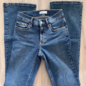 Blå bootcut jeans från Gina Tricot strl 32 - Snygga blå bootcut jeans från Gina Tricot i strl 32 med klassisk femficksdesign och mid waist. Jeansen har en lätt tvättad look och raka, utsvängda ben. Tillverkade i mjukt denimtyg som sitter skönt hela dagen. Stretch 