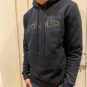 Mörkblå Dondup hoodie  - Snygg mörkblå hoodie från Dondup med stor logga framtill. Klassisk känguruficka, huva med snörning och ribbade muddar. Perfekt för dig som gillar stilrena och bekväma plagg med premiumkänsla.