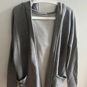 Grå hoodie-kofta med huva och fickor - Mysig grå hoodie-kofta med öppen front, stora fickor och huva. Perfekt för lager-på-lager och chill dagar