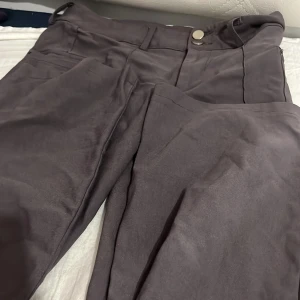 Grå kostymbyxor från SHEIN i storlek S - Snygga grå byxor från SHEIN i storlek S med klassisk passform och raka ben. Byxorna har fickor fram och stängs med knapp och dragkedja. Perfekta för en clean och stilren look. Materialet känns mjukt och har en lätt glans.