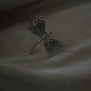 Silverfärgad ring med trollslända - Unik ring i silverfärgad metall formad som en trollslända. Vingarna har en snygg textur som ger extra detalj och cool känsla. Perfekt för dig som gillar naturinspirerade smycken och vill sticka ut med något annorlunda.