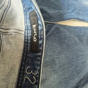 Blå jeans från Replay, storlek 32 - Säljer ett par klassiska blå jeans från Replay i storlek 32. Jeansen har raka ben, snygga slitningar och tydliga sömmar på bakfickorna. Perfekta för dig som gillar en tidlös och avslappnad look. Materialet är robust denim i bomull.
