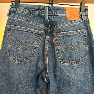 Levi's 501 blå jeans W26 L32 - Klassiska Levi's 501 jeans i blå denim med raka ben och hög midja. Jeansen har knäppning med knappar, fem fickor och ikoniska detaljer som läderpatch och röd Levi's-tagg bak. 