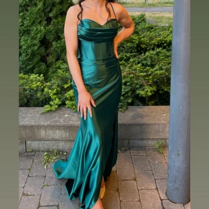 Grön lång satinklänning med snörning - Bara använd en gång, i nyskick. Originalpris: 3000 kr Säljes för: 1200 kr (pris kan diskuteras) Storlek: XS/S