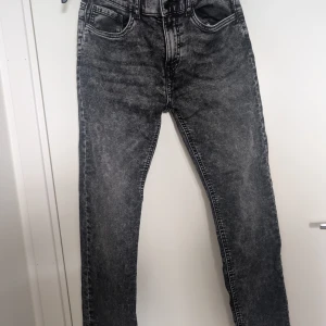 Svarta tvättade raka jeans, regular 164 - Snygga svarta jeans med tvättad look och raka ben. Klassisk femficksmodell med normal passform och midja. Perfekta för dig som gillar en avslappnad men stilren vibe. Materialet är jeans och färgen är mörkgrå till svart. Strl 164 motsvarar xs i herr. Regular fit. Som Nya! Endast provade två gånger. 