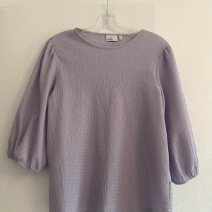 Ljuslila blus från Isolde - Supersöt ljuslila blus från Isolde med trekvartsärmar och lätt puff vid axlarna. Tillverkad i ett strukturerat tyg som ger en cool känsla. Perfekt att styla med jeans eller kjol för en fräsch look.