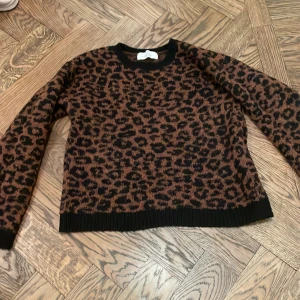 Leopardmönstrad stickad tröja H&M - Säljer en brun och svart stickad tröja från H&M med leopardmönster. Tröjan har rund halsringning, ribbade muddar och lång ärm. Storlek 140
