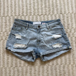 Ljusblå ripped jeansshorts  - Snygga ljusblå jeansshorts från Samsøe Samsøe med slitna detaljer och upprullade benslut. 100% bomull, perfekt för sommardagar. Shortsen har normal passform och stängs med knapp och dragkedja. Köpta i nyskick från sellpy och aldrig använda av mig!