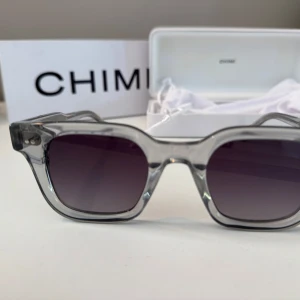 Grå 04 solglasögon CHIMI - Snygga solglasögon från CHIMI modell 04 med transparent grå båge och rektangulär form. Glasen är mörka med en cool tonad effekt. Kommer med originalväska och putsduk. Nypris 1250kr. Endast använda ett fåtal gånger.