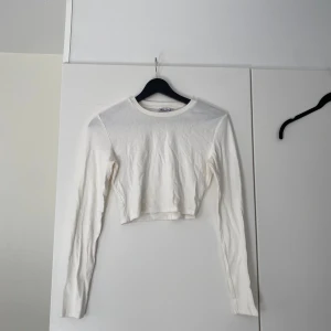 Vit croppad långärmad topp från Zara - Säljer en stilren vit croppad topp från Zara i storlek M. Toppen har långa ärmar och är tillverkad i mjuk bomull, perfekt att matcha med jeans eller kjol för en enkel och fräsch look.