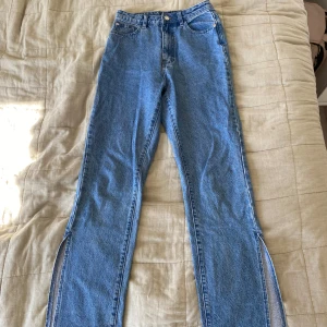 Blå jeans med slits från Missguided - Säljer ett par blå jeans från Missguided i klassisk denim med hög midja och raka ben. Byxorna har snygga slitsar nertill på båda benen som ger en trendig vibe. Perfekta för dig som vill ha något extra till din outfit.