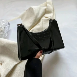 Svart axelväska  - Snygg svart axelväska med croco-mönstrad yta och stilren form. Väskan har en smal axelrem och stängs med dragkedja. Perfekt storlek för det viktigaste och ger en trendig vibe till din outfit.