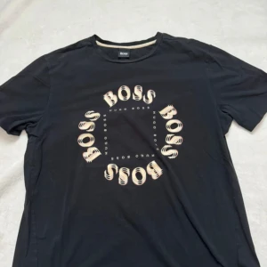 Svart t-shirt och shorts set från HUGO BOSS - Svart t-shirt från Hugo Boss i bomull med coolt tryck där det står BOSS i en cirkel på bröstet. Klassisk rund halsringning och korta ärmar. Perfekt för dig som gillar stilrena och trendiga plagg med tydlig logga.