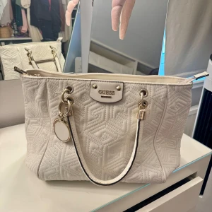 Vintage handväska Guess - Jättefin handväska från Guess, har även axelremmar som går att ta av. Den är väldigt rymlig med flera fack och små detaljer (berlocker) som går att ta av och på. Väskan har ytterst små deffekter vid handtag och baksida. Skriv för fler bilder.