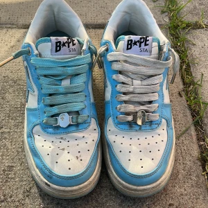 Jätte bra skor och kan få massa brudar med de skojar inte  - BAPE STA sneakers i en fräsch kombo av ljusblått och vitt med klassisk stjärndesign på sidorna. Skorna har snörning, perforerad tå och platt sula. Ovandelen är i glansigt syntetmaterial och insidan är vit. Perfekta för dig som gillar streetwear och vill sticka ut.